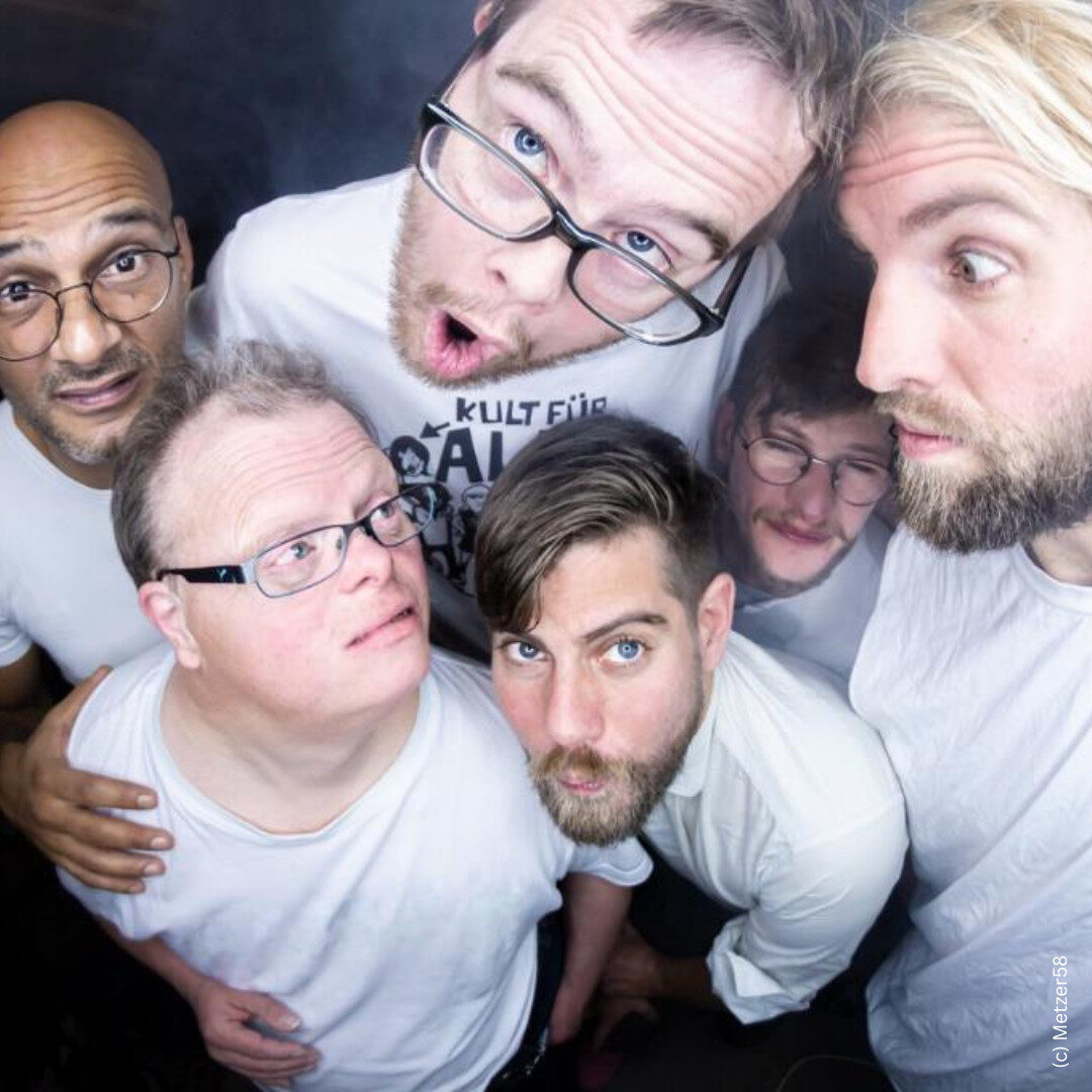 Foto von der Band Metzer58. Sechs Männer stehen eng beieinander und schauen fröhlich und neugierig in die Kamera. Sie tragen überwiegend weiße Kleidung.